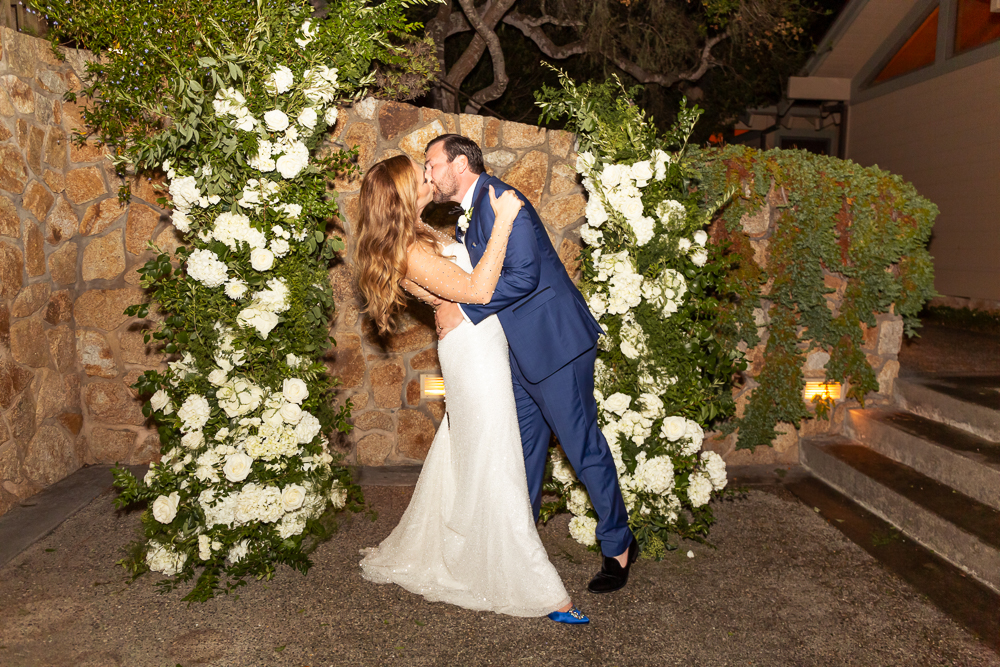groom dips bride opulent white floral arch
