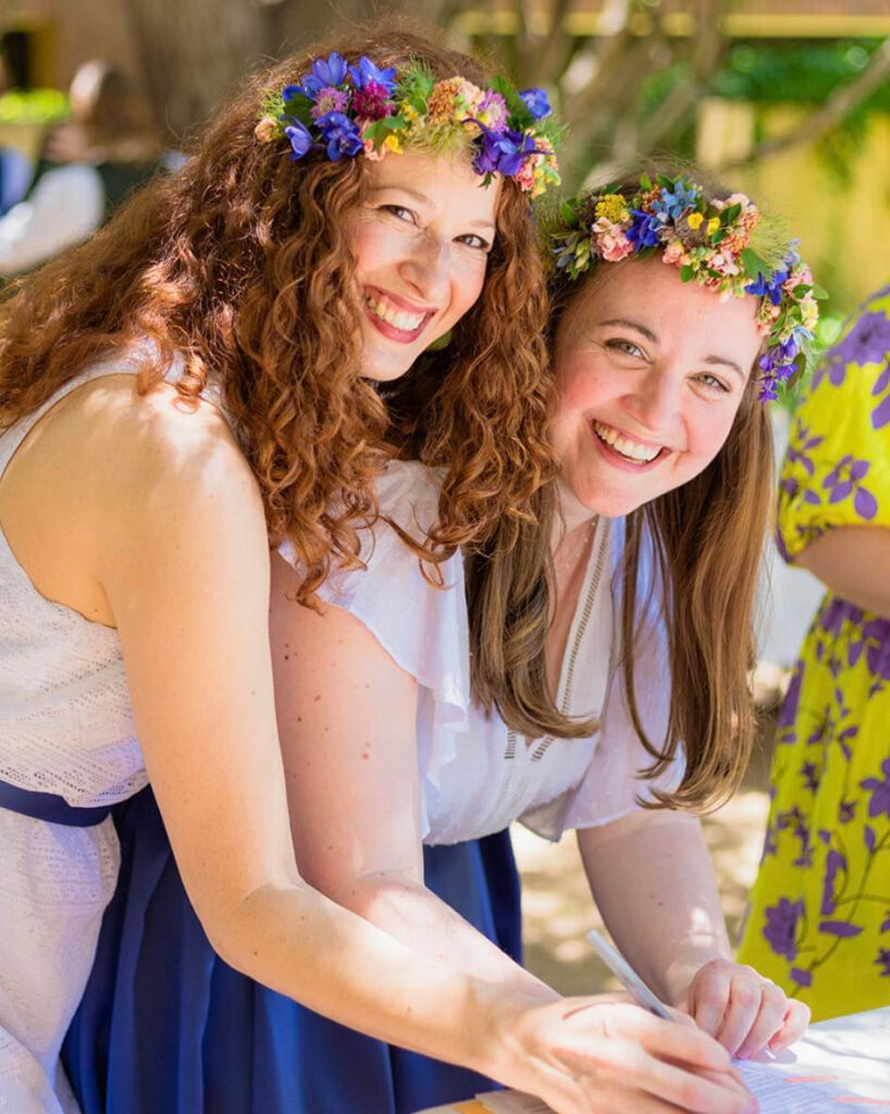 Two fresh newlyweds smiling and wearing flower tiaras