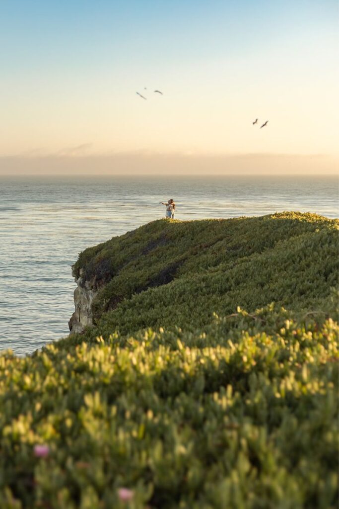 a couple standing on a cliff and looking at the ocean