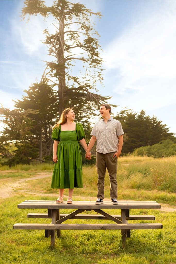 A couple standing on a picnic table and posing for their Santa Cruz engagement photos