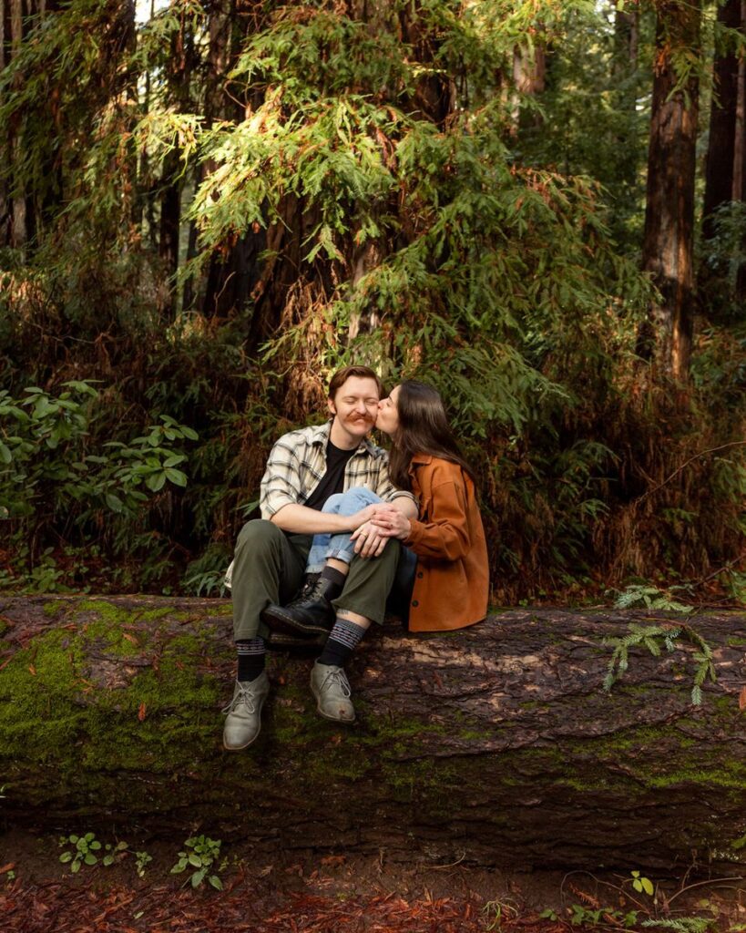 A couple sitting and kissing on a fallen log