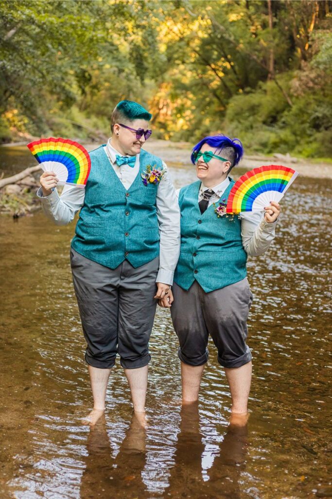 Nova and Arden posing with funky sunnies and rainbow fans for their neurodivergent wedding