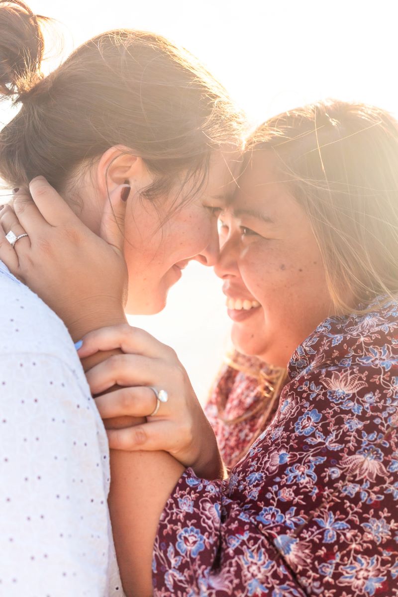 Couple leaning in close to each other and smiling you can see the engagement rings of both 