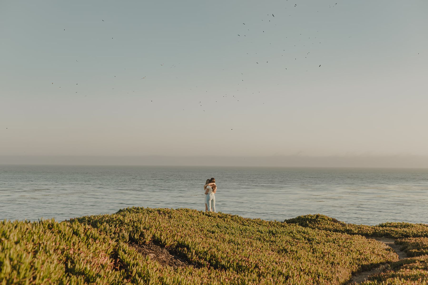 Two women embracing on a cliff looking at the ocean