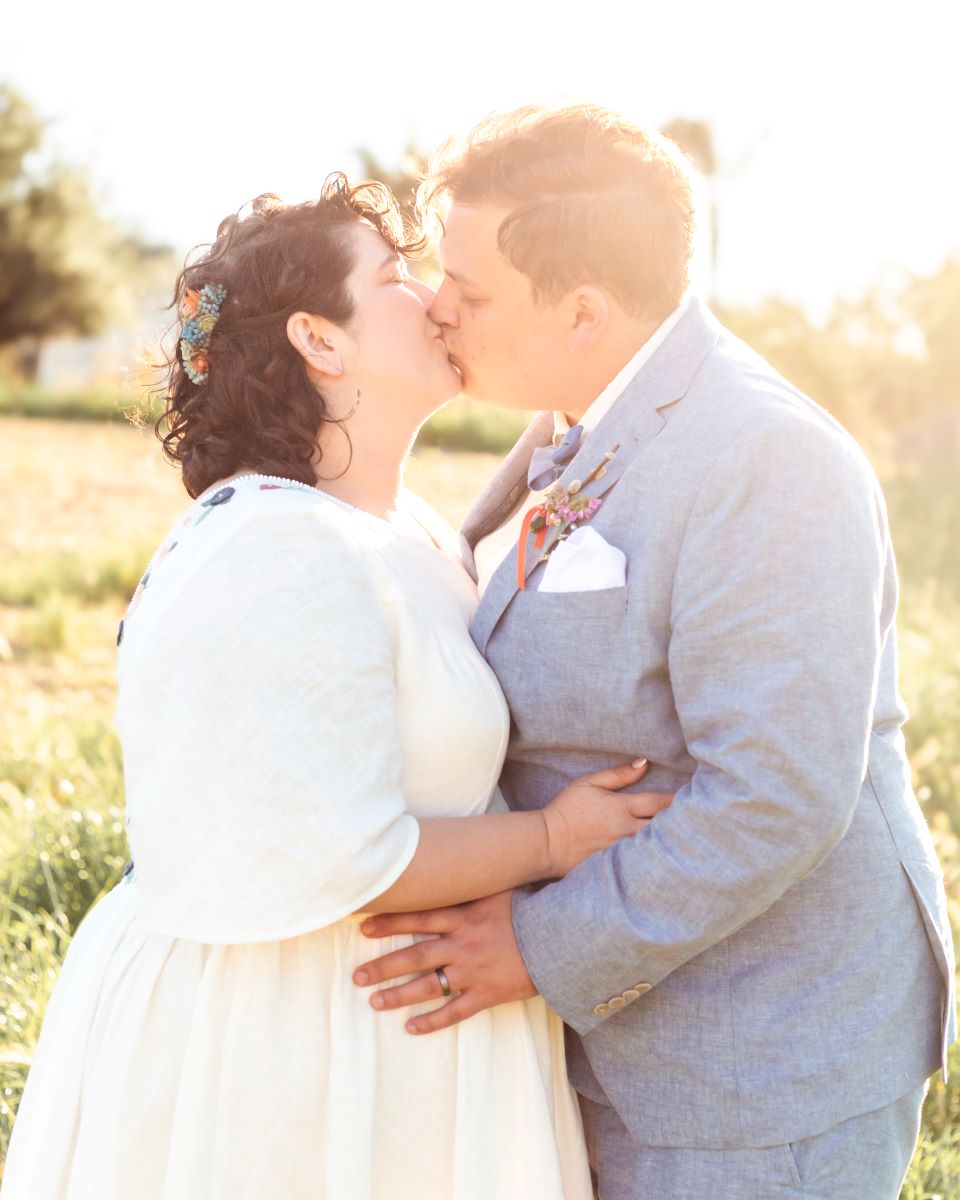 A couple kissing each other one is wearing a white wedding dress and the other has on a gray tuxedo 