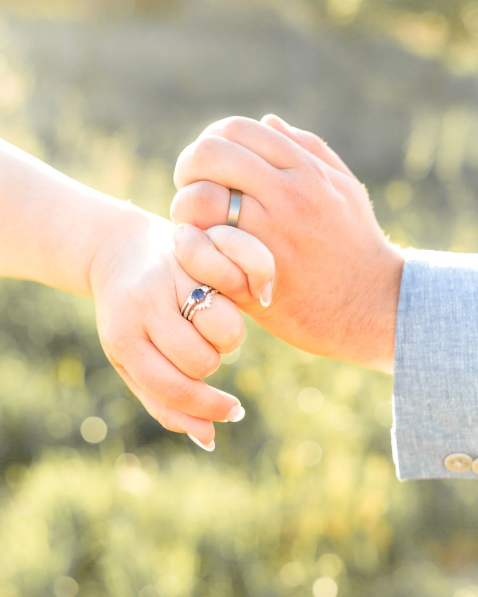 A couple holding pinkie fingers and showing off their wedding rings 