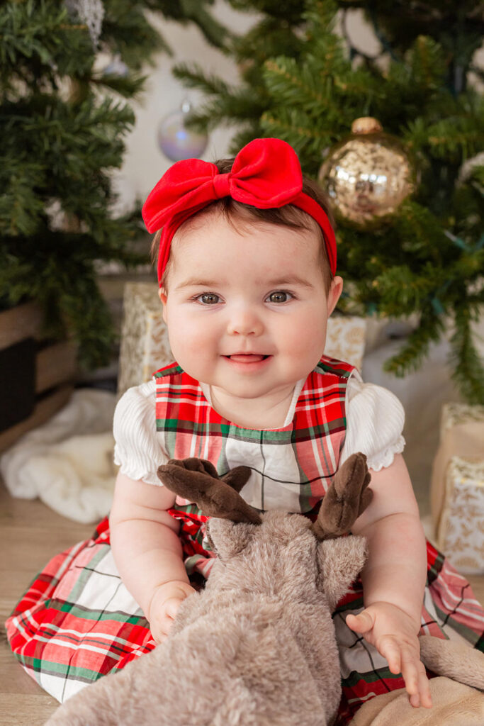 A child sits on the ground with a red bow smiling.