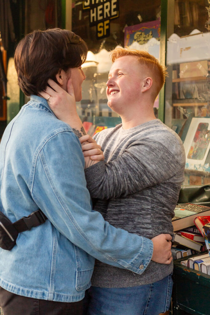 A couple standing close together with one holding the other's waste and one with their hand on the other's cheek. 