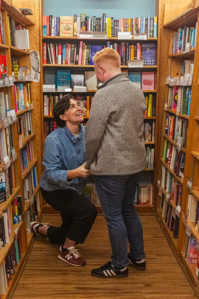 A person kneeling down in a bookstore proposing to their partner 