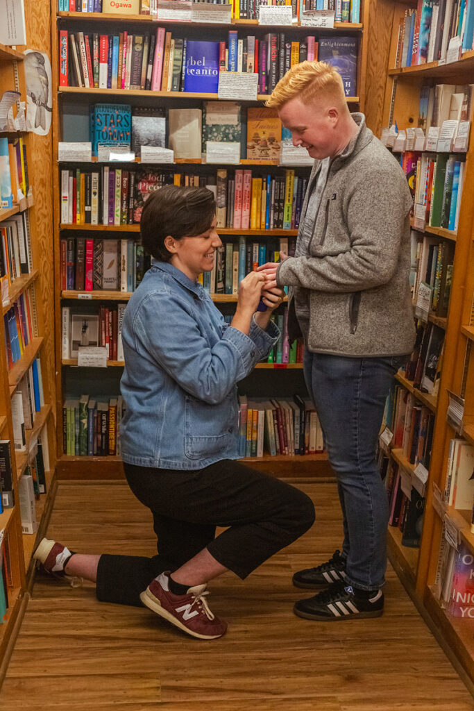 A person on one knee putting an engagement ring on their partner's finger 