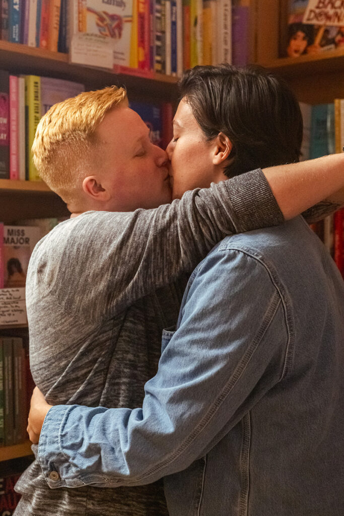 A couple kissing in a bookstore with their arms around each other 
