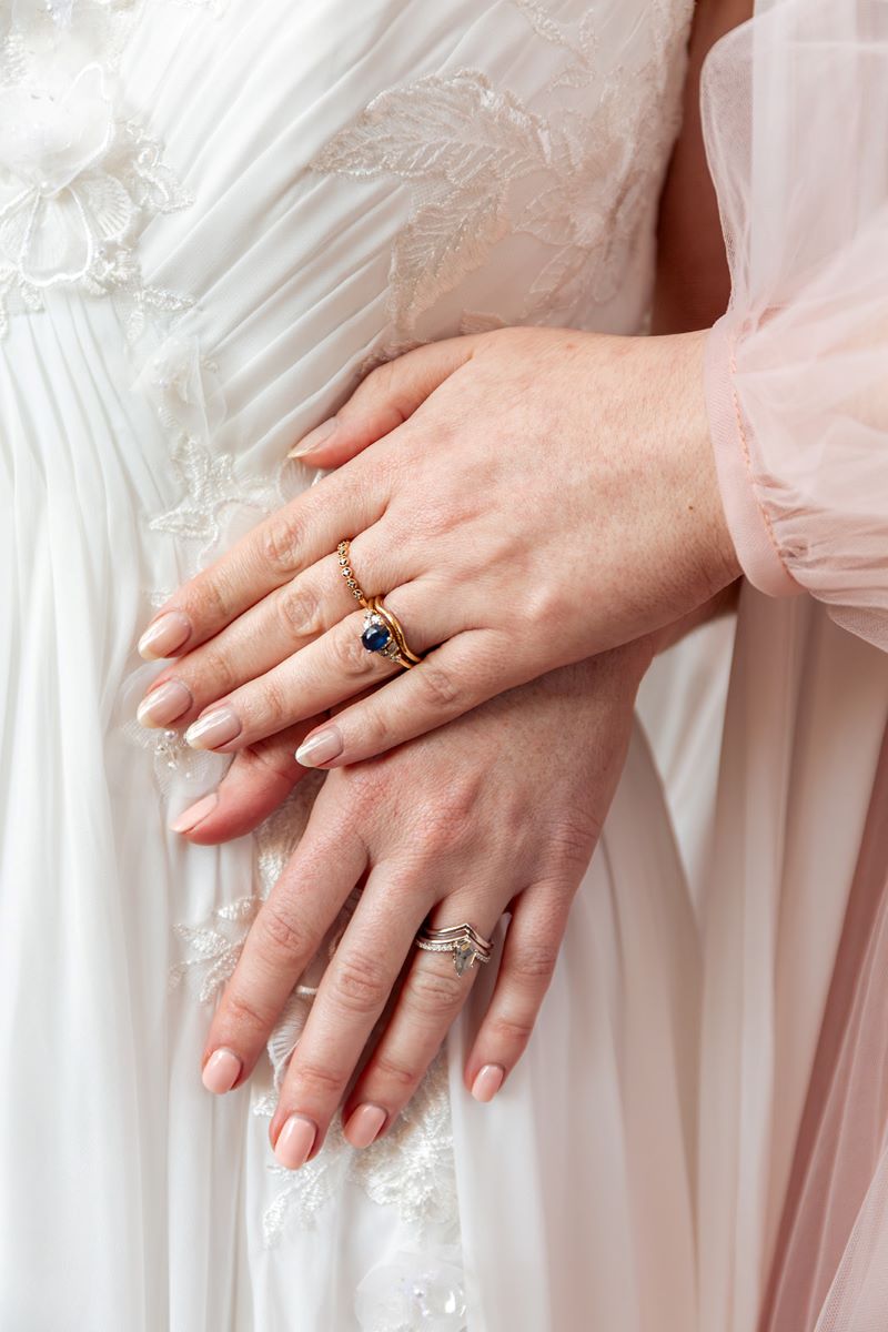 A couple showing off their wedding rings one is wearing a pink gown and the other is wearing a white gown 