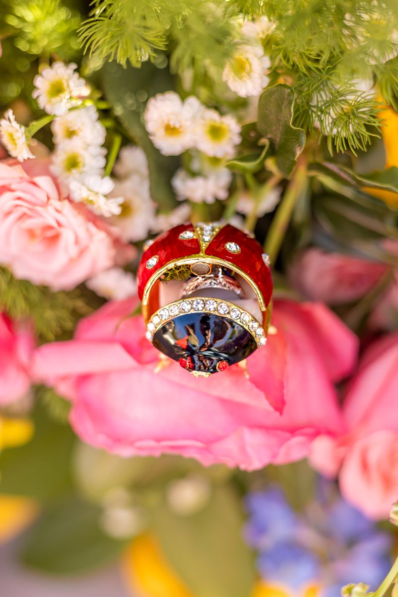 An ornately decorated ladybug box featuring a diamond ring inside and perched on top of a bouquet of flowers