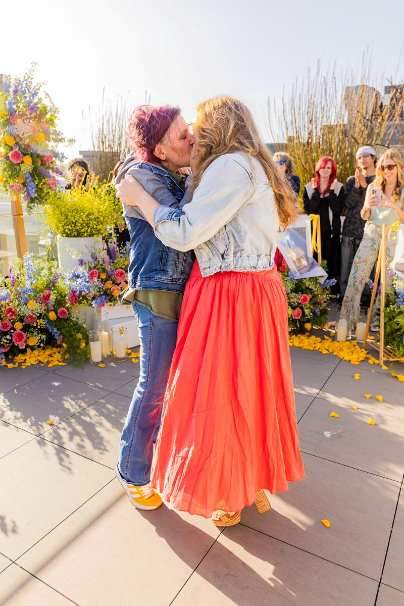 a couple kissing on the rooftop of biteunite in san francisco surrounded by their family and friends