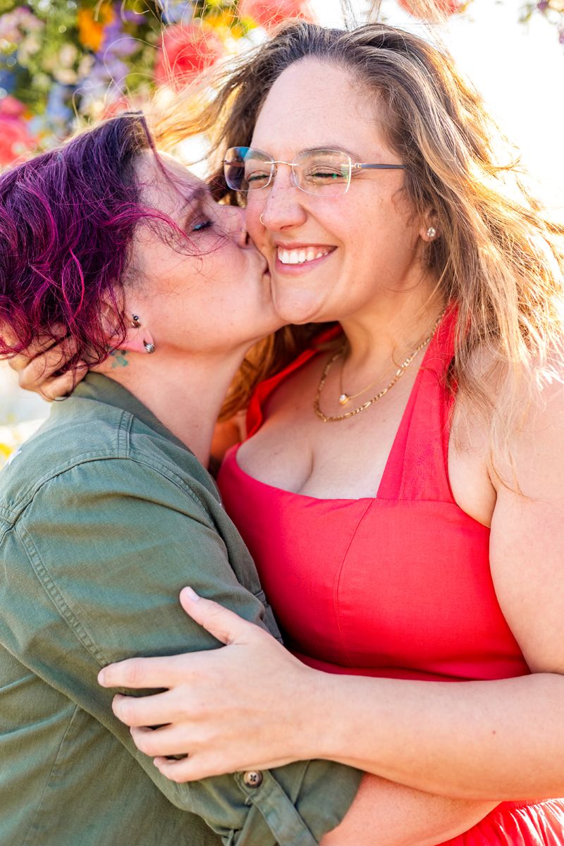 a queer couple celebrating their engagement one is kissing the other on the cheek