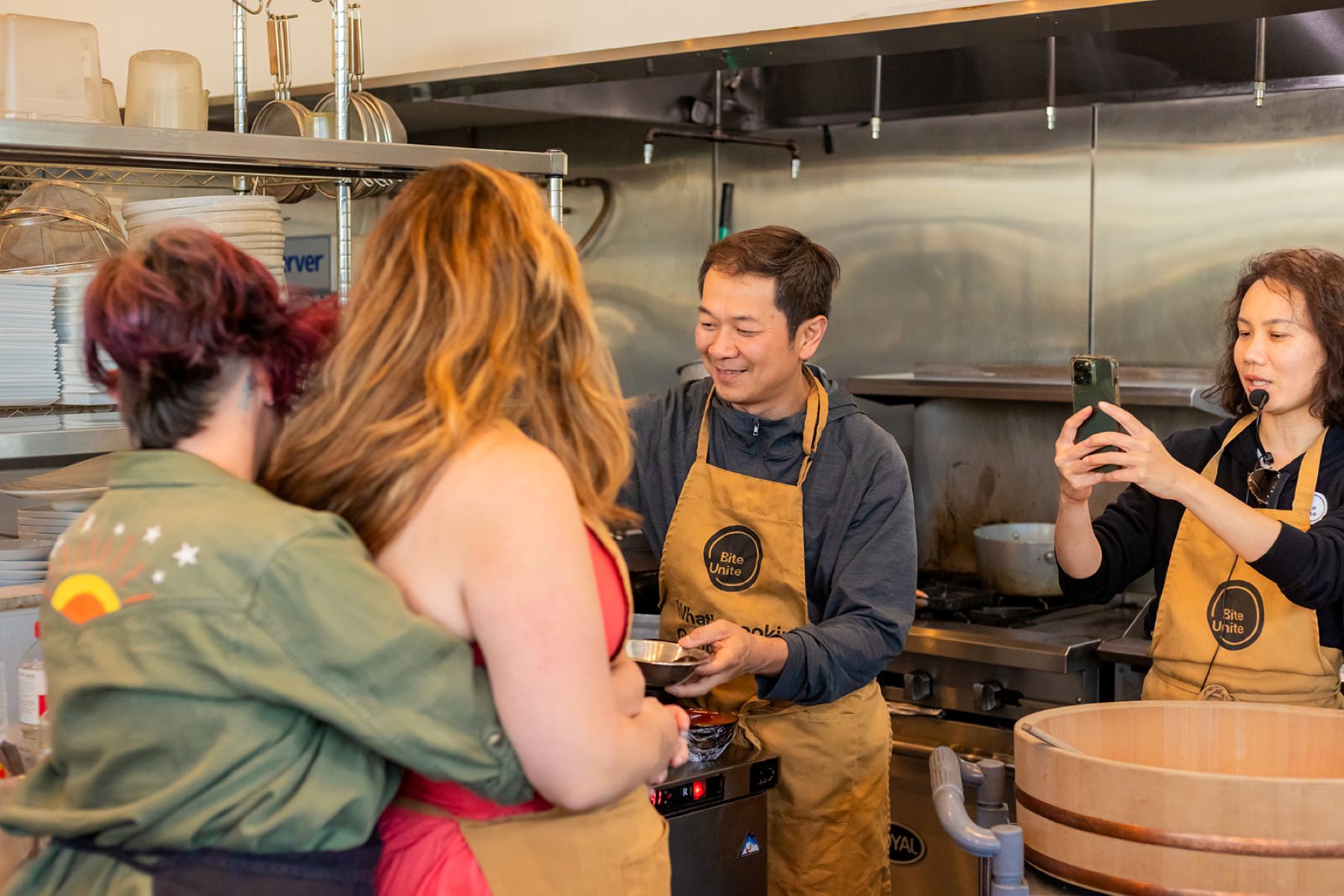 a couple in a sushi making class at biteunite one is embracing the other from behind as they watch the instructor