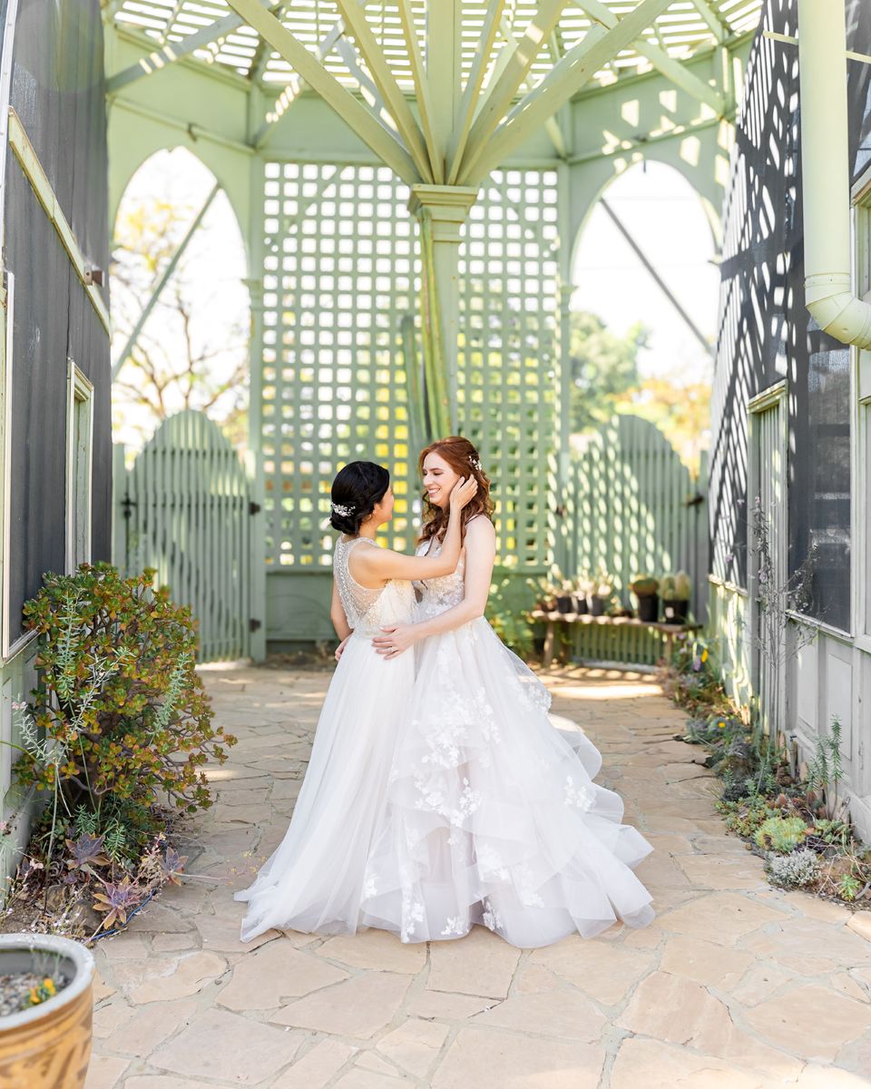 two women in white wedding dressses inside of a gazebo at ruth bancroft garden embracing each other
