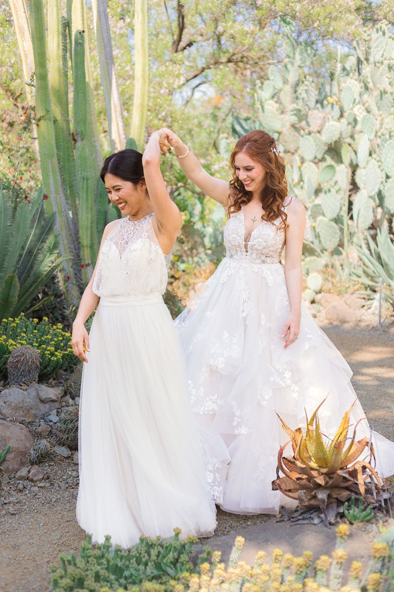 two women inside of ruth bancroft gardens one woman is spinning the other they are both wearing white wedding dresses