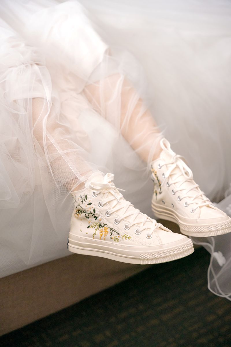 a woman wearing white sneakers stiched with a floral design