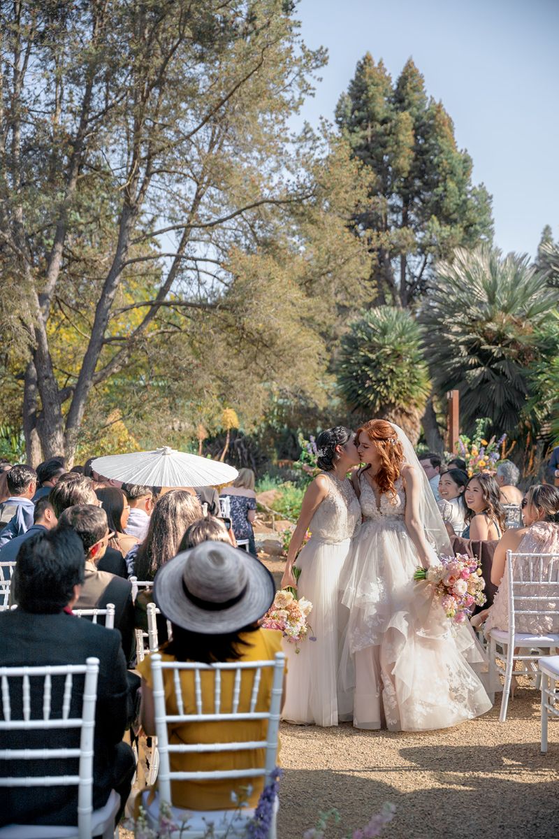 two women kissing after their wedding ceremony at ruth bancroft garden as their guests cheer for them