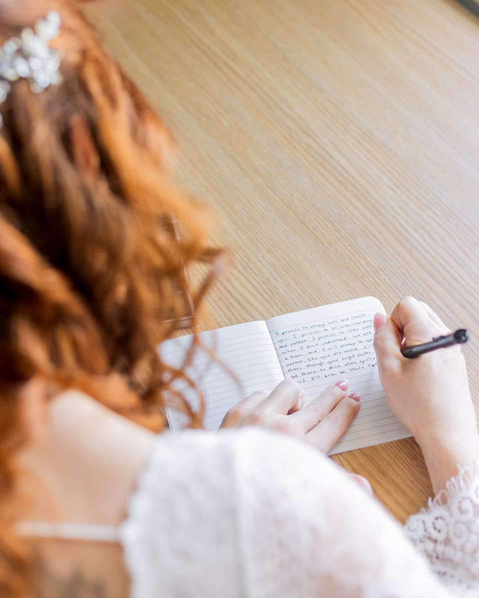 a woman sitting at a table writing her wedding vows in a journal