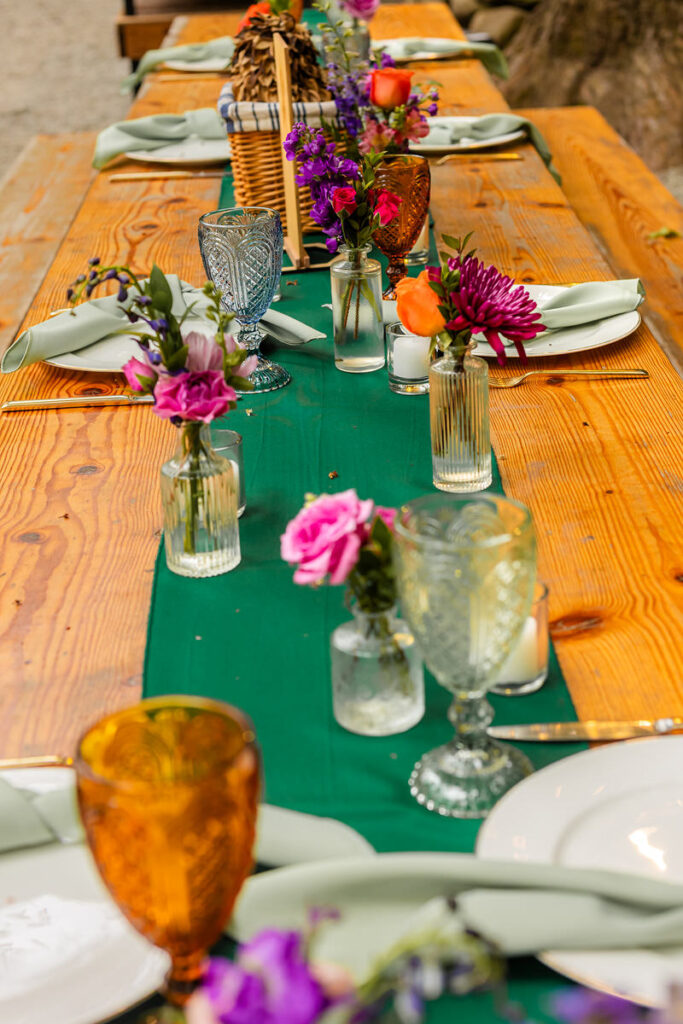 Small flower arrangements, glassware and a small green tablecloth on a wooden table