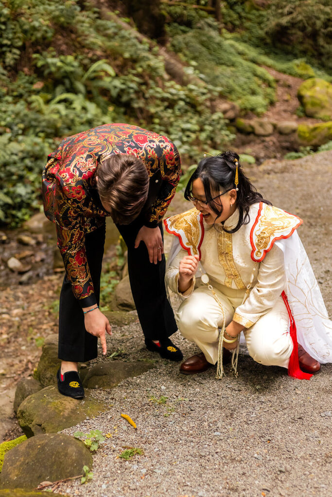 A couple leaning down and looking at an insect in the woods