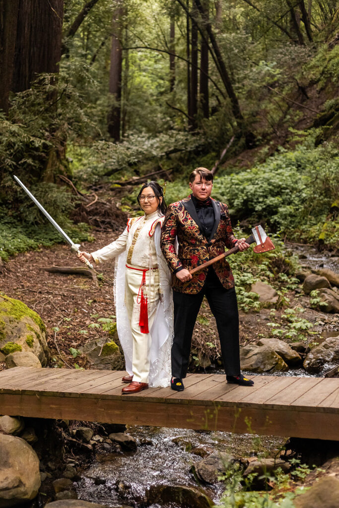 A wedding couple standing back to back holding a sword and an axe