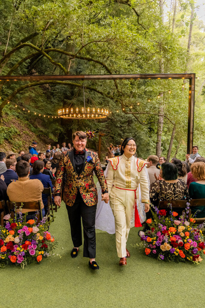 A newlywed couple holding hands and walking back up the aisle after their wedding