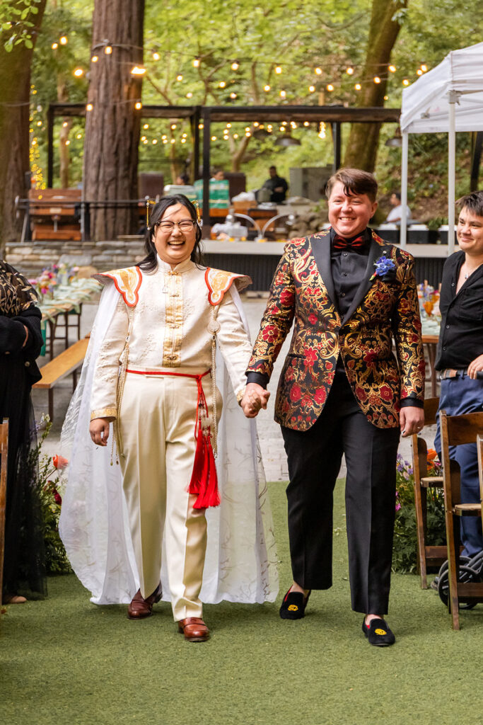 A newlywed couple smiling and holding hands as they walk together