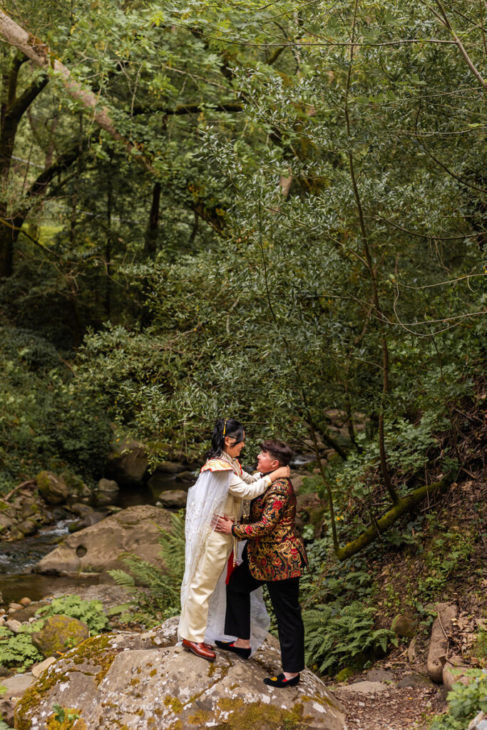 A newlywed couple standing on a rock with their arms around each other