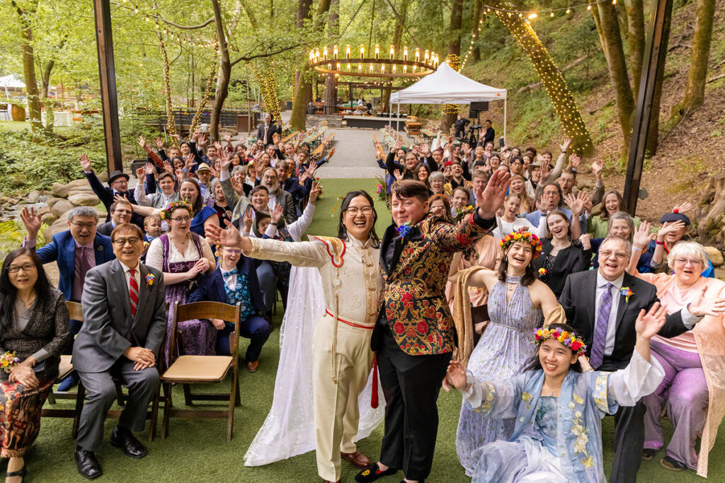 newlywed couple celebrating with their wedding guests cheering in their chairs behind them