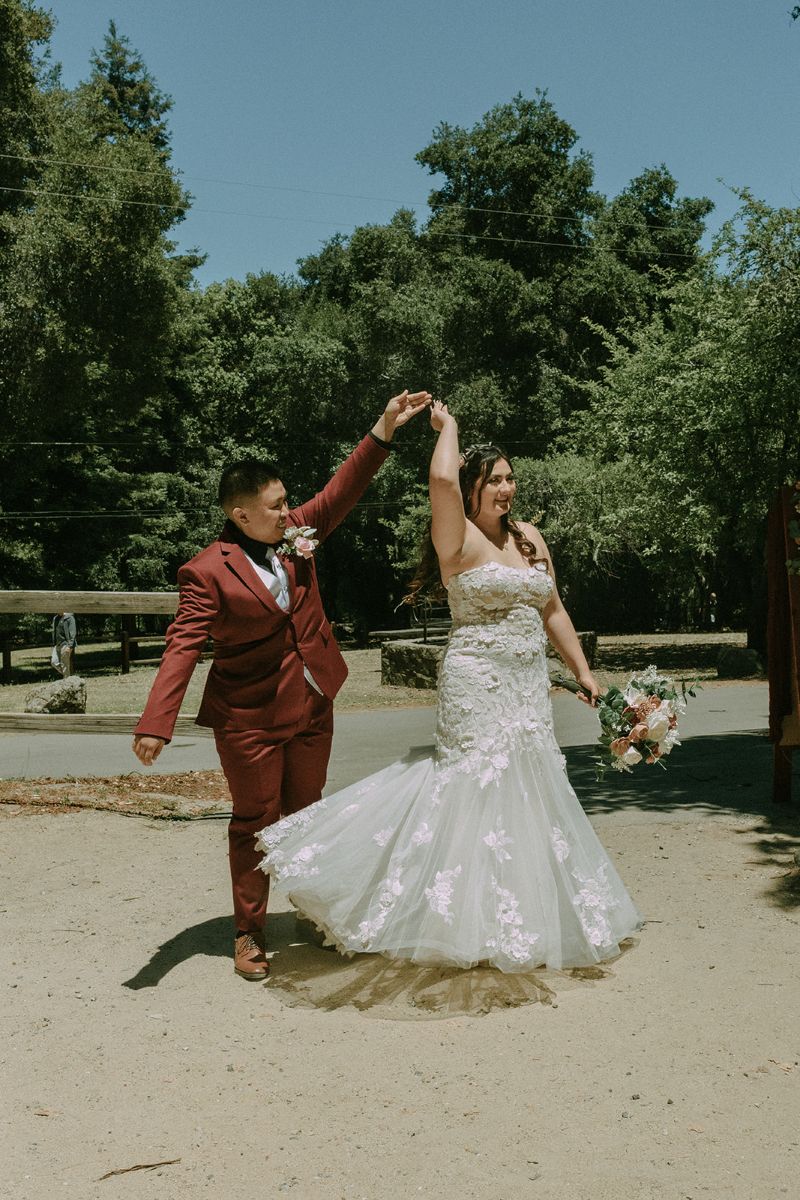 a couple dancing together outdoors one is spinning the other and one is wearing a red suit the other is wearing a white wedding dress and holding a bouquet of flowers