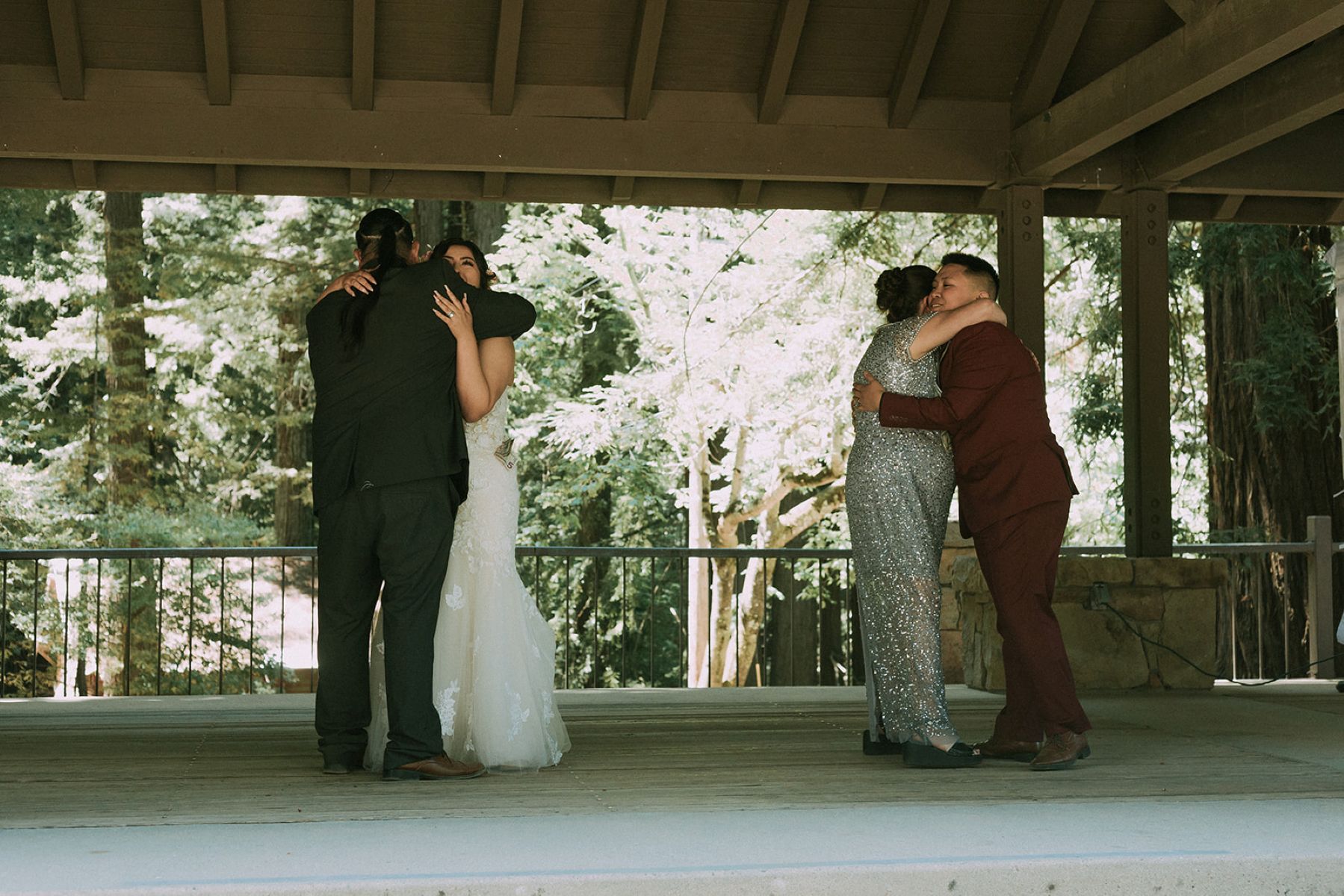 a queer couple sharing a dance on a stage outdoors with their parents