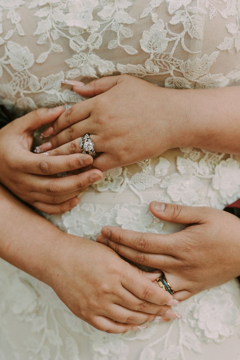 a couple showing offer their wedding rings one is hugging the other from behind