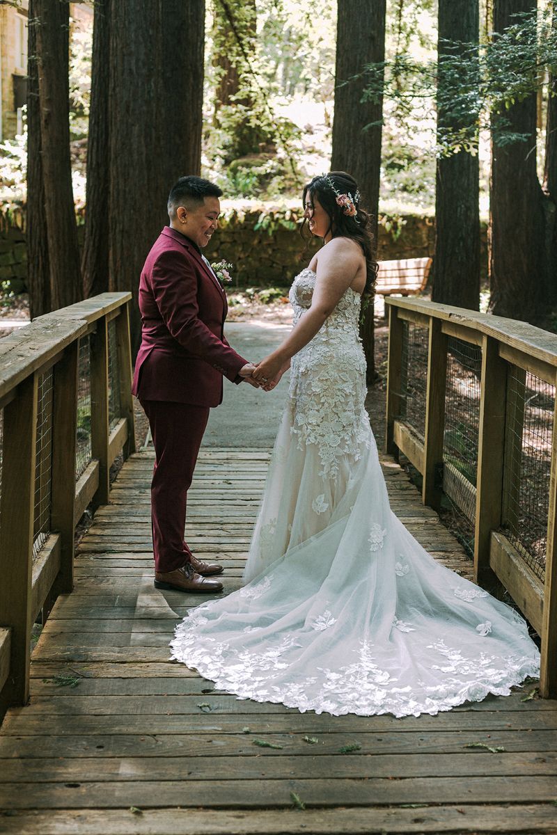 a couple sharing a first look on a bridge holding hands with each other one is wearing a red suit and the other is wearing a white wedding dress