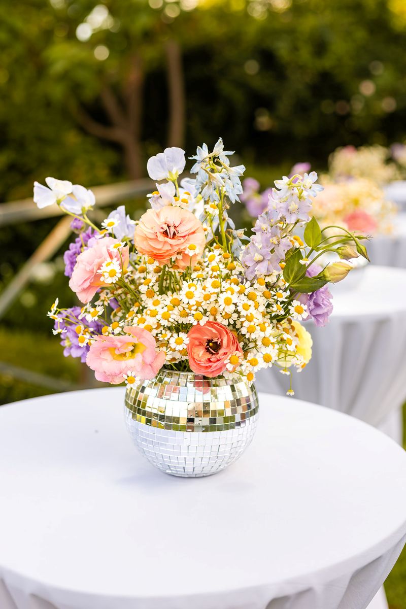 a table with a white tablecloth on top of it is a floral bouquet in a disco ball 