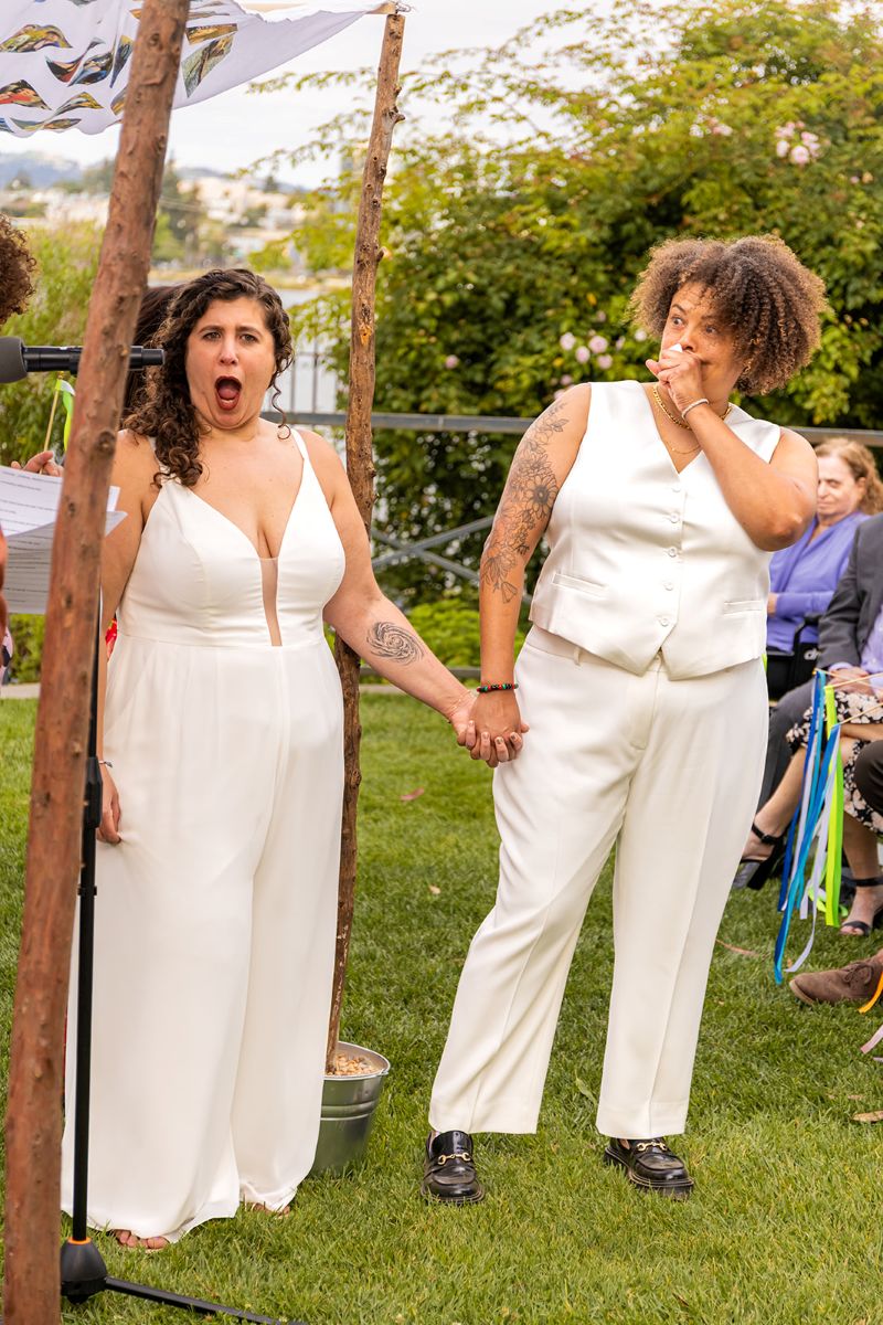 a couple looking in surprise at the camera and holding hands 