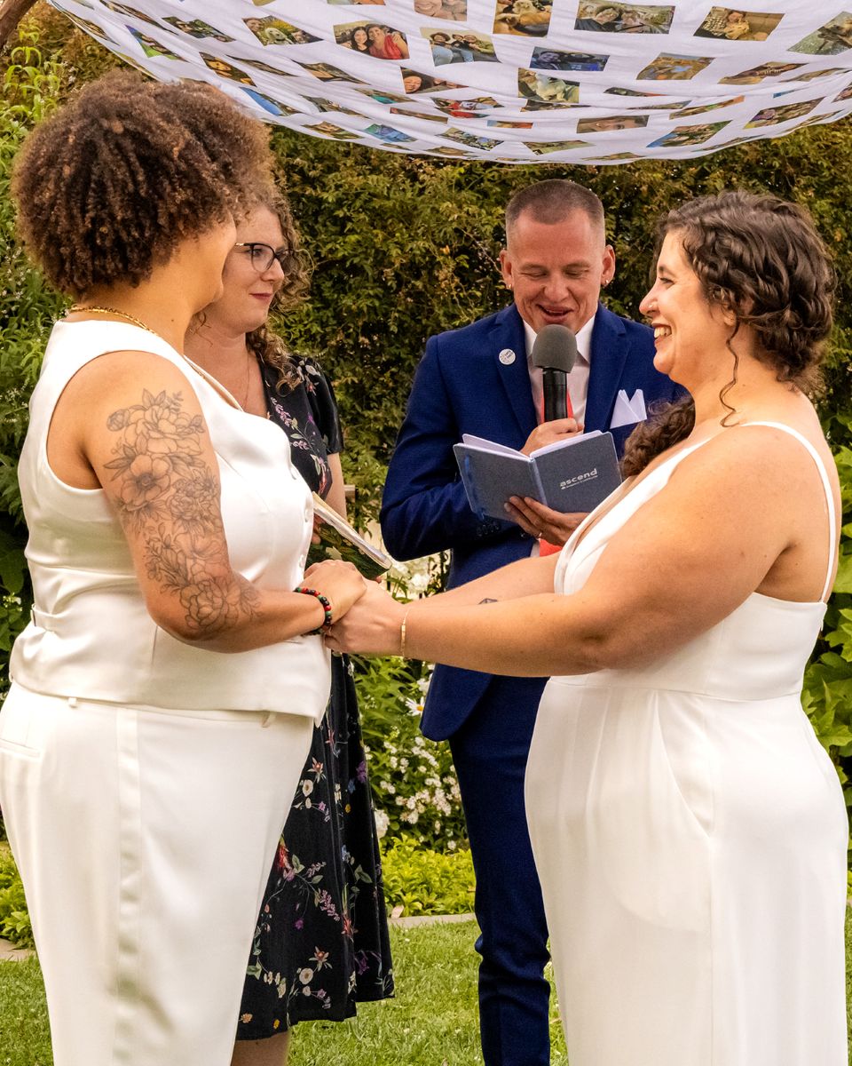 a couple having their wedding ceremony at camron stanford house they are holding hands and smiling as their officiant reads from a book 