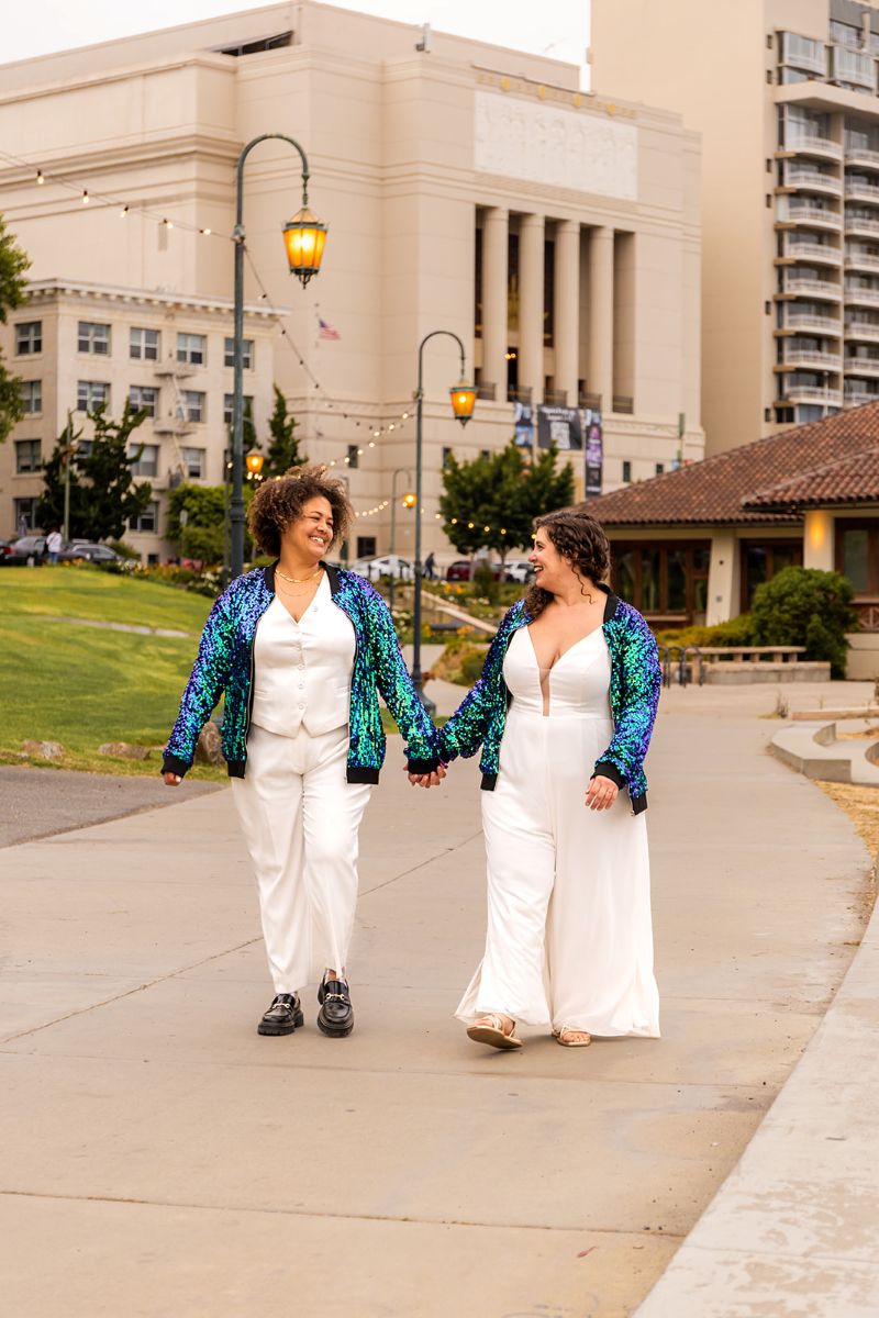 a couple walking hand in hand wearing matching jackets down a street in oakland california
