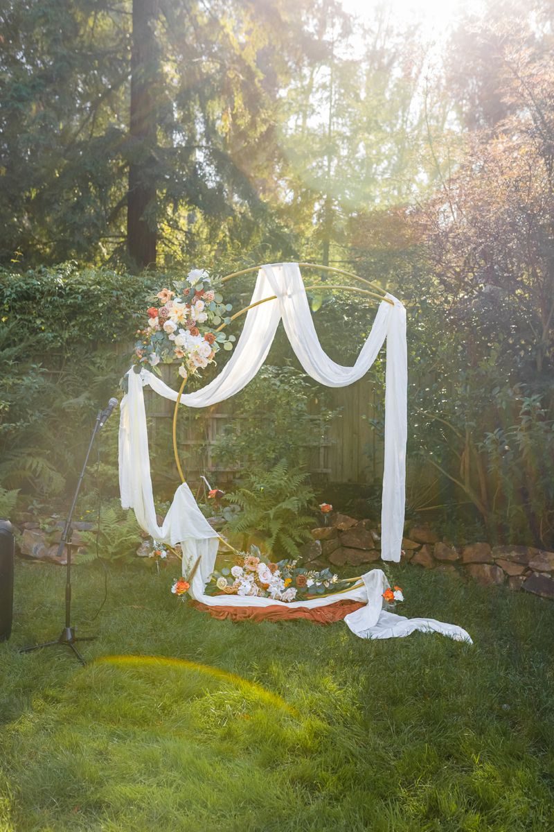 a moon shaped arch in the garden at fern cottage set up for a wedding surrounded by trees 