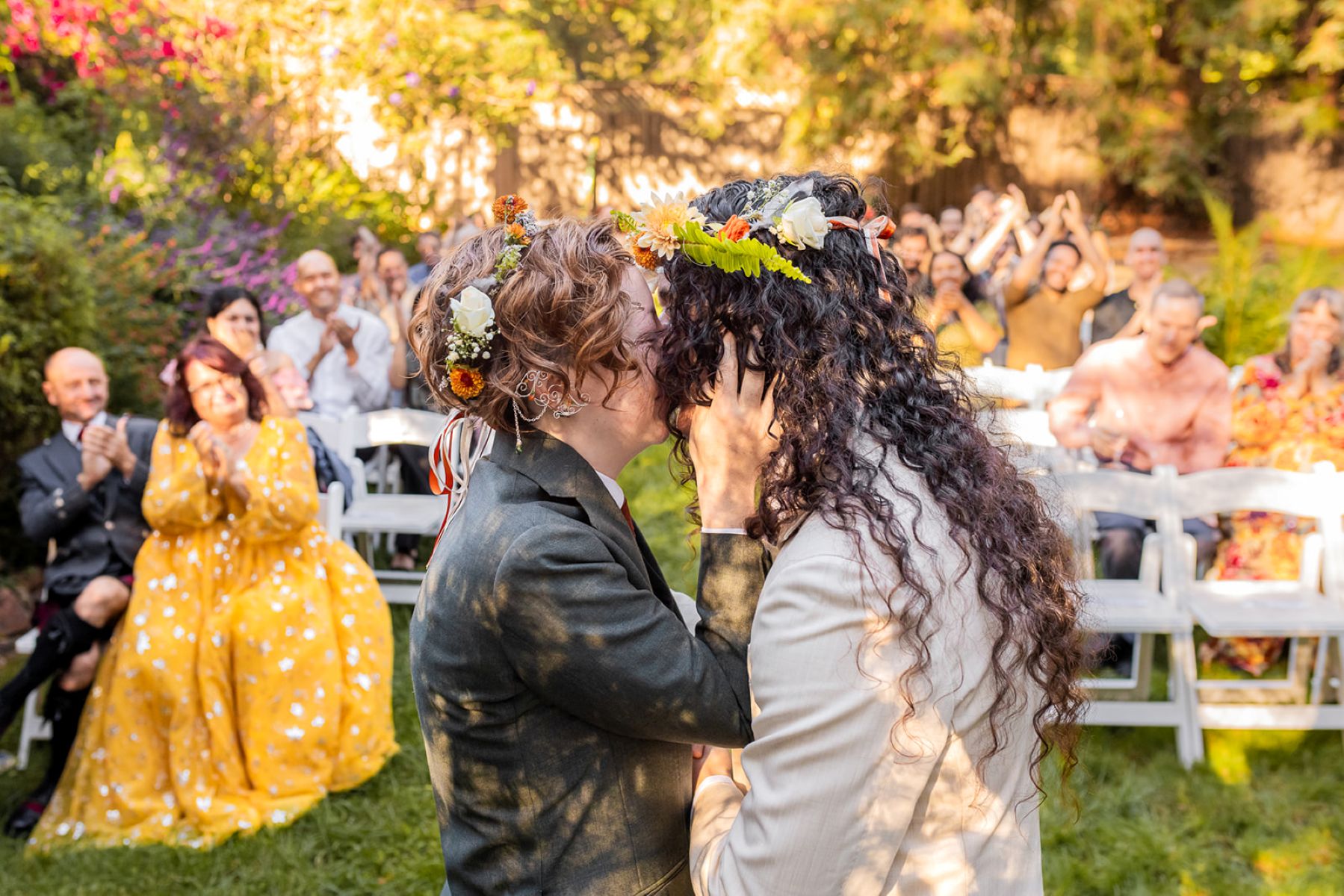 a couple kissing at their wedding ceremony at fern cottage in el sobrante as their wedding guests cheer for them