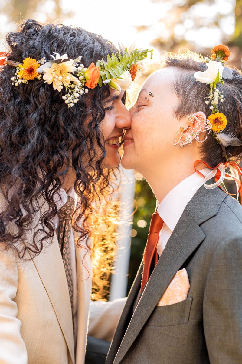 a couple leaning in for a kiss at their wedding ceremony they are both wearing flower crowns 