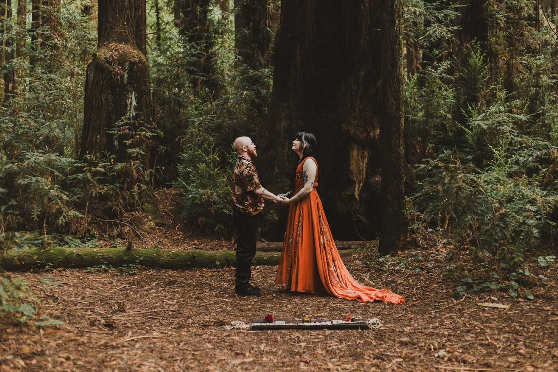 a couple having a wiccan wedding ceremony at henry cowell state park they are holding hands and surrounded by the woods 
