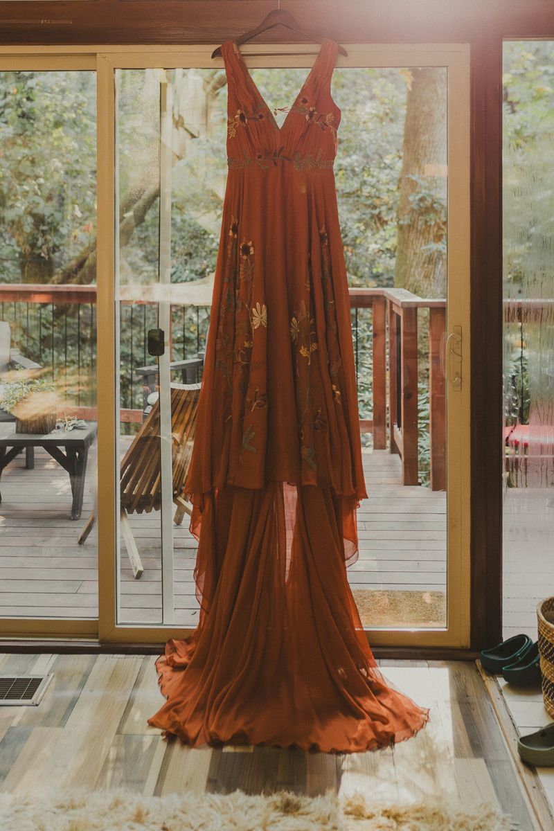 a vibrant orange wedding dress hanging on a hook next to a porch deck 