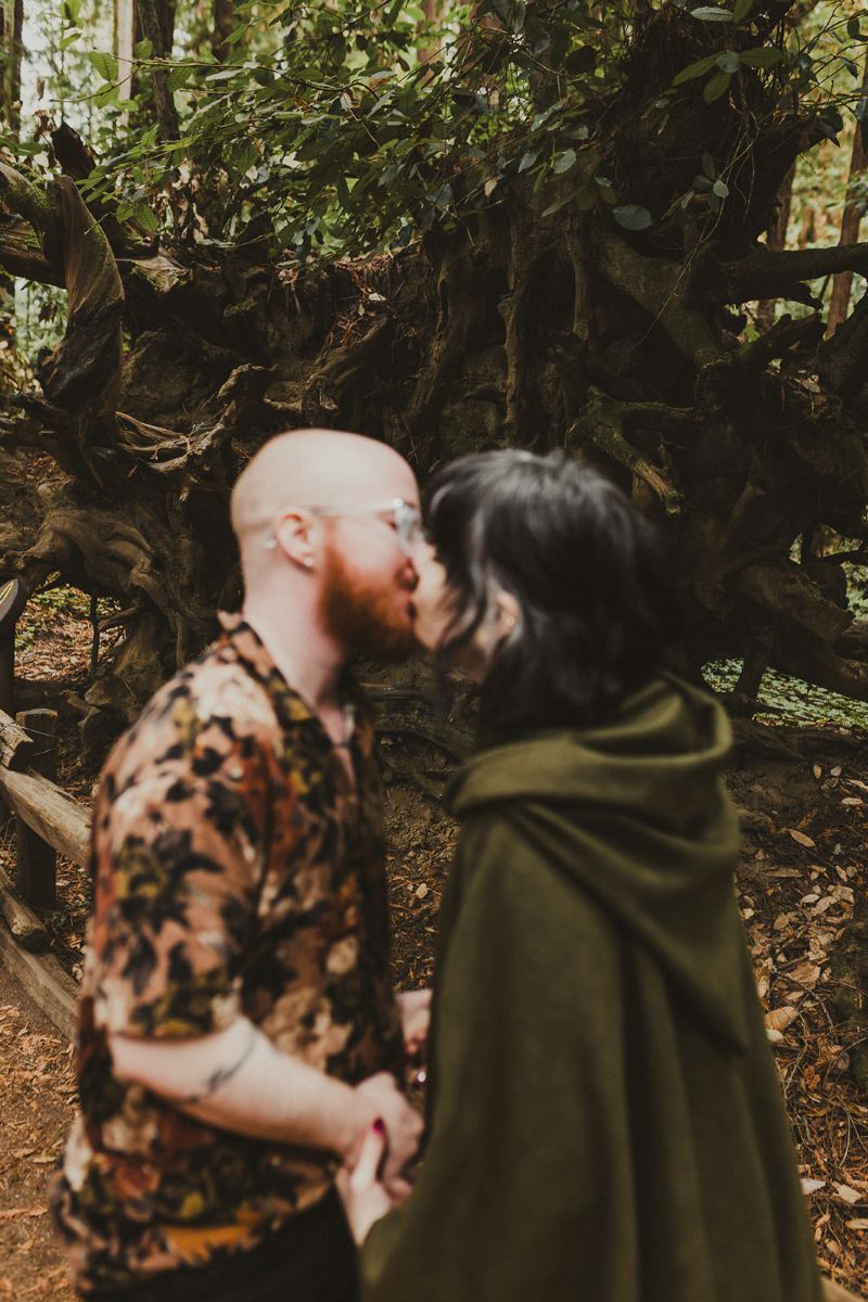 a couple kissing and holding hands in henry cowell state park surrounded by the forest 