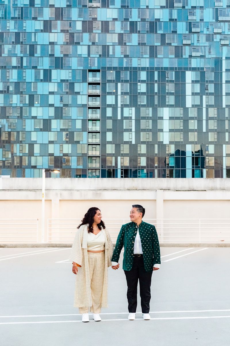 a couple holding hands and smiling at each other one is wearing an indian inspired outfit 