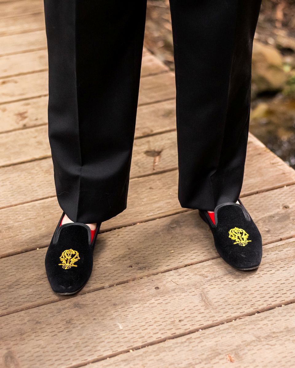 a person wearing black pants and black shoes adorned with a gold symbol standing on a wooden bridge 