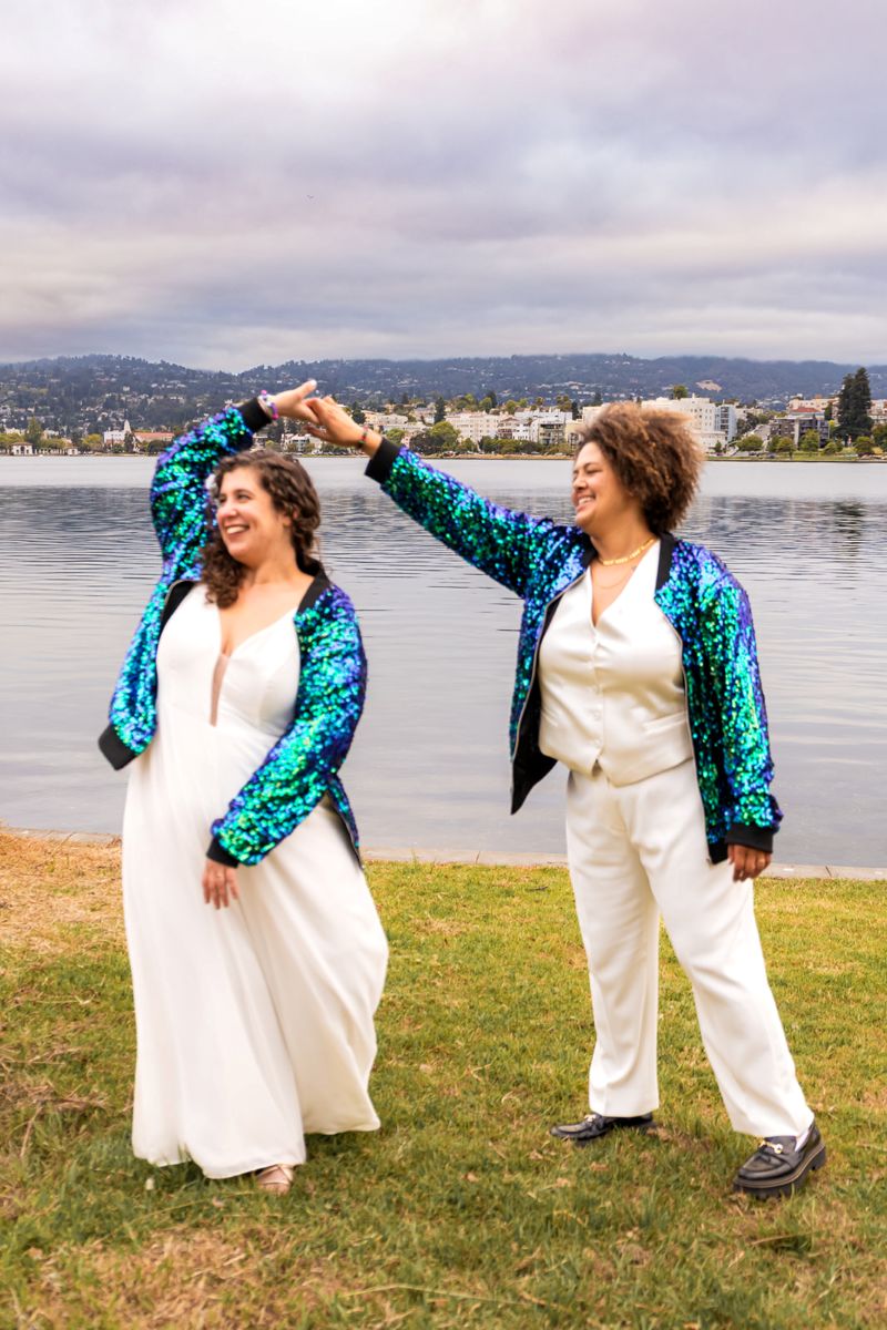 a copule standing next to the water wearing matching sparkly sequin jackets one is spinning the other 