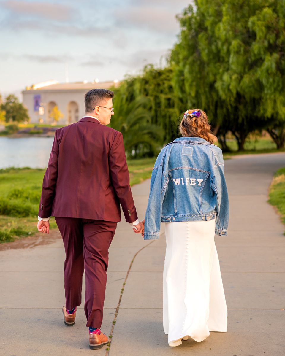 a couple holding hands walking on a path together one is wearing a blue jean jacket that says wifey the other is wearing a burgundy jacket 